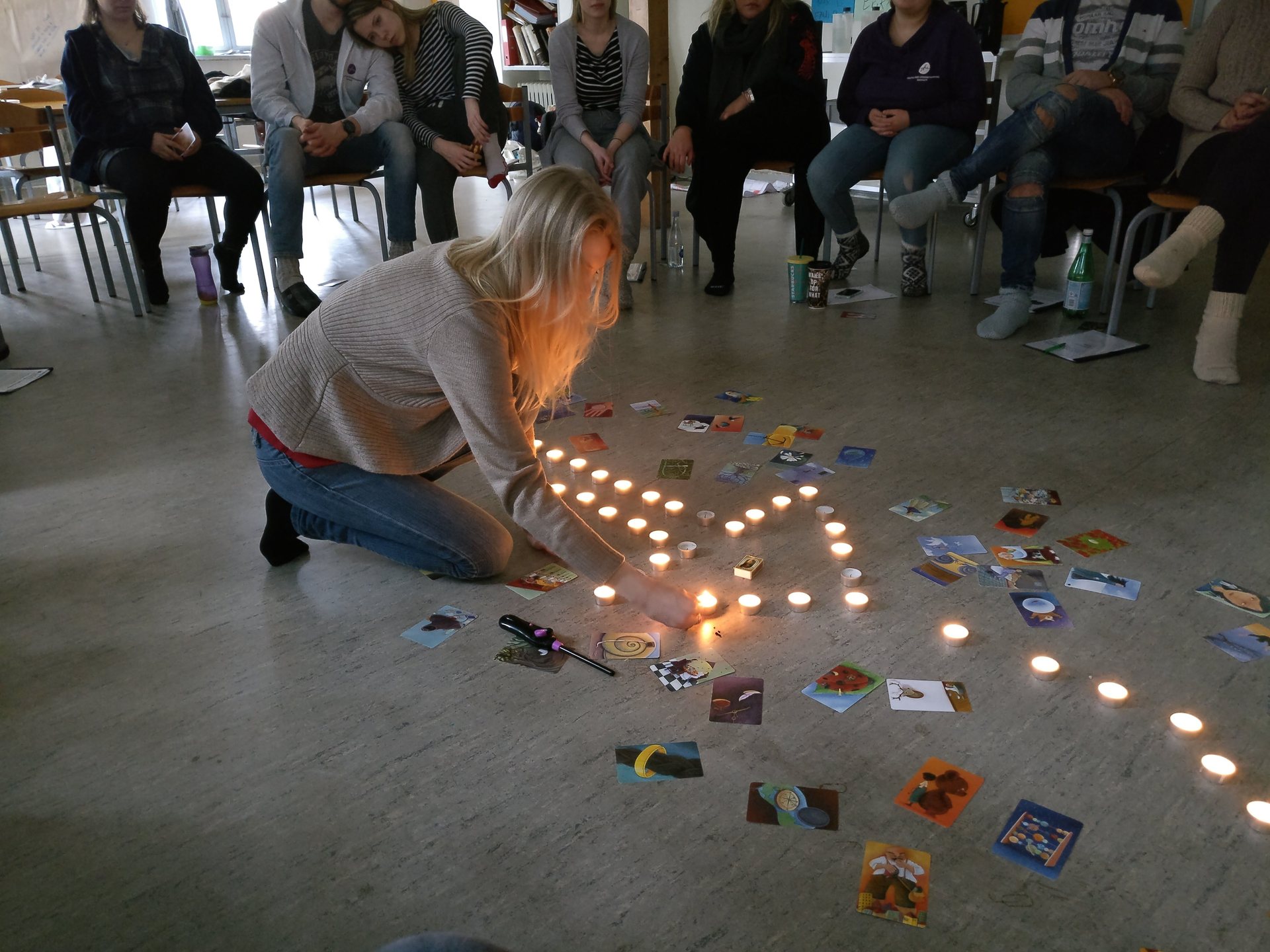 A participant kneeling to light a line of tea lights laid out on the floor among scattered picture cards