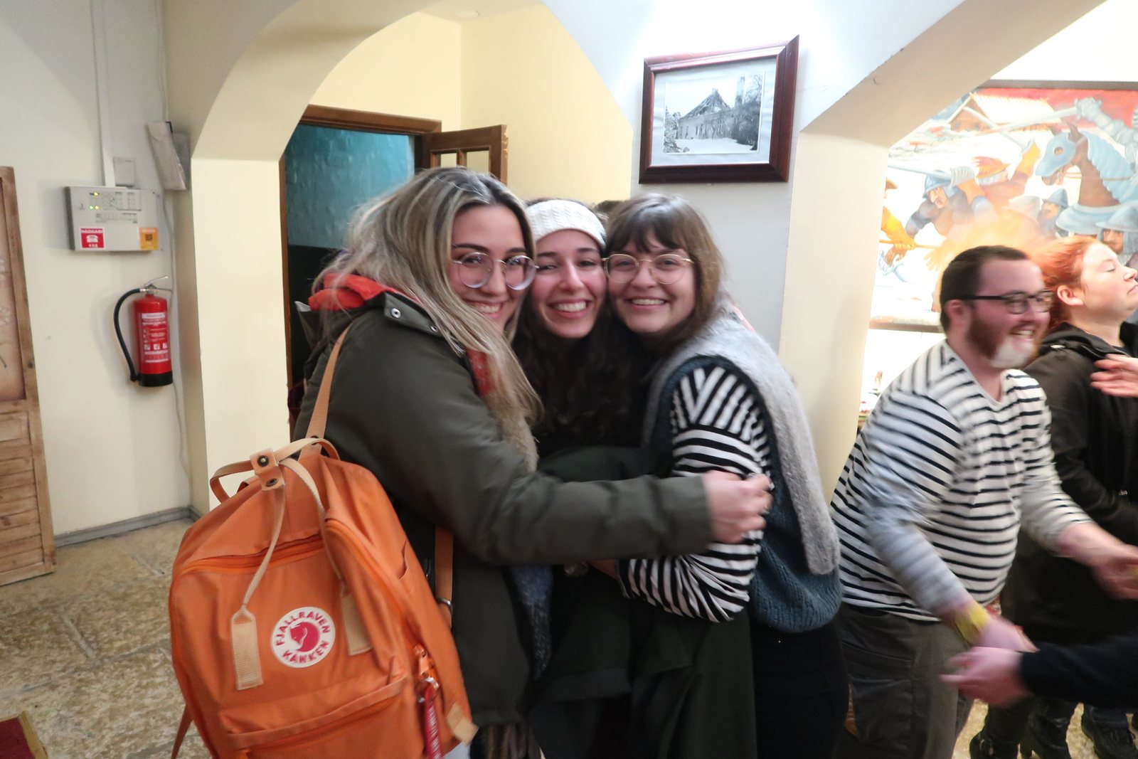 Three participants laughing in a long hug, with others gathered around them
