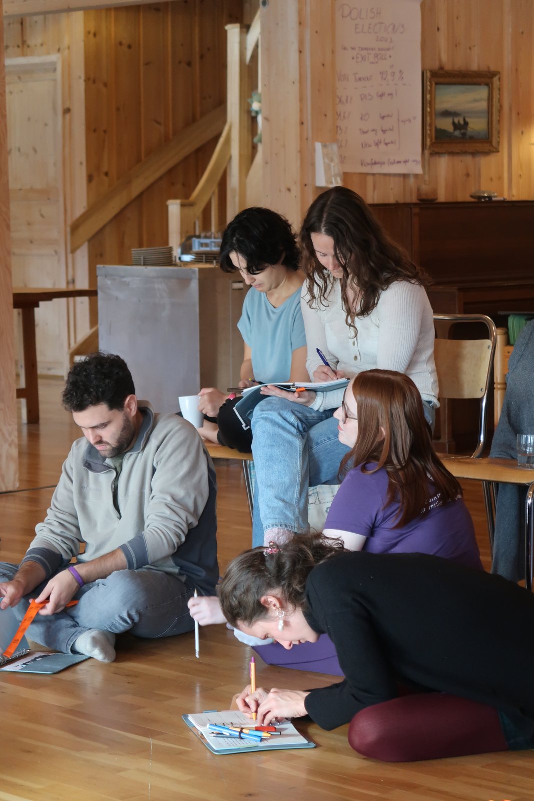 Participants working together on the floor and around a table in a bright wooden room