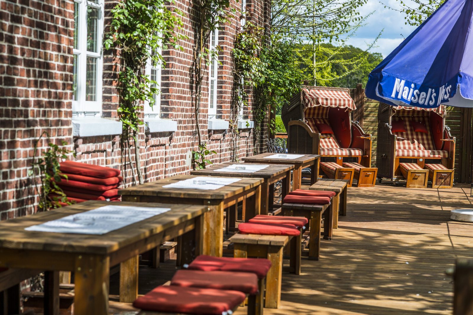 Long wooden tables with red cushions set out along the brick facade