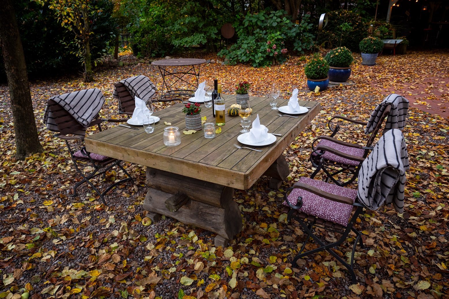 A long wooden table laid for dinner in a garden covered in autumn leaves