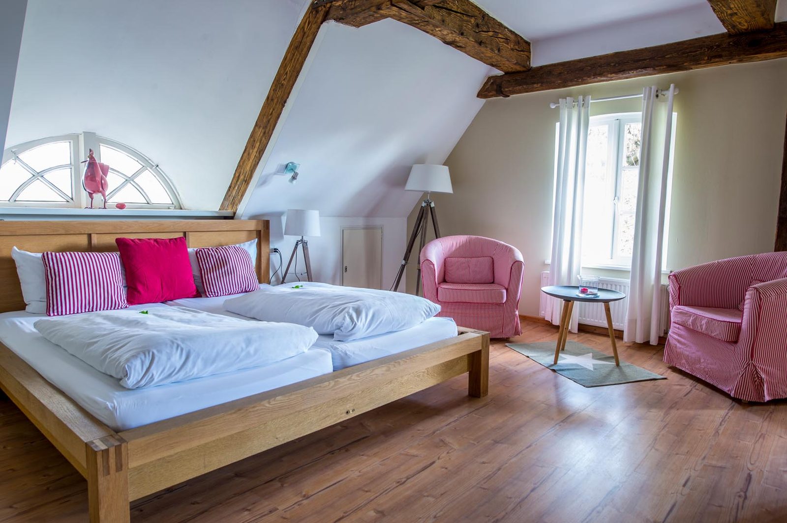 A bedroom under a sloping beamed ceiling with a dormer window